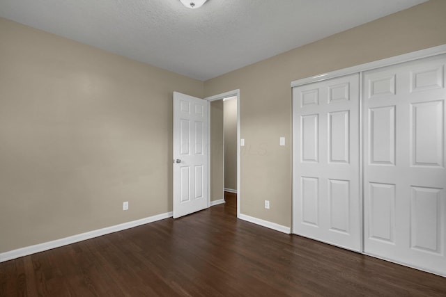 unfurnished bedroom with a closet, a textured ceiling, dark wood-type flooring, and baseboards