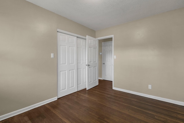 unfurnished bedroom featuring dark wood-style floors, a closet, a textured ceiling, and baseboards