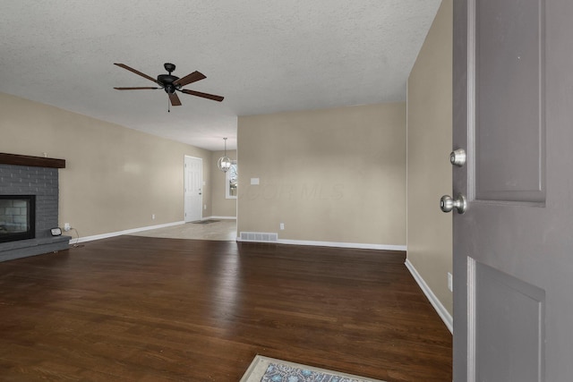 unfurnished living room featuring wood finished floors, visible vents, ceiling fan, a textured ceiling, and a brick fireplace