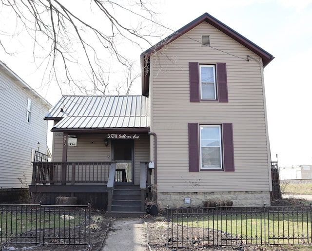 traditional-style home featuring a standing seam roof, covered porch, a fenced front yard, and metal roof