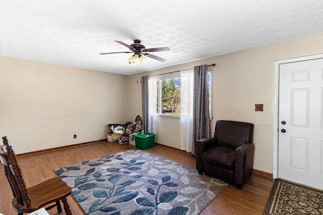 living area with a textured ceiling, wood finished floors, baseboards, and ceiling fan