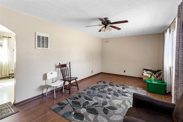 sitting room with baseboards, ceiling fan, wood finished floors, arched walkways, and a textured ceiling