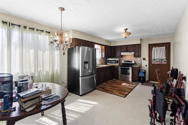 kitchen featuring a notable chandelier, under cabinet range hood, a sink, stainless steel appliances, and dark brown cabinetry