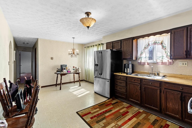 kitchen with wallpapered walls, light countertops, stainless steel refrigerator with ice dispenser, a textured ceiling, and a sink