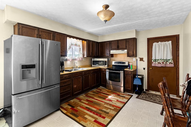 kitchen with under cabinet range hood, light floors, stainless steel appliances, and light countertops