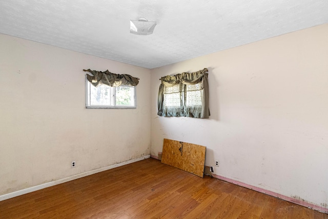 unfurnished room with a textured ceiling, baseboards, and wood finished floors