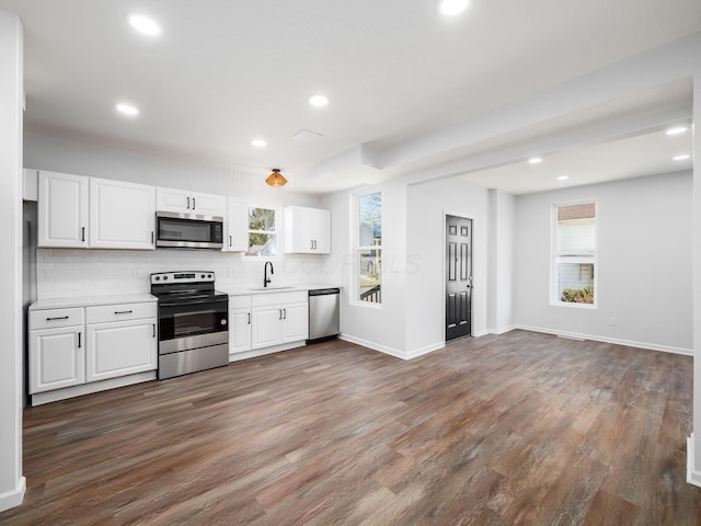 kitchen with a sink, dark wood finished floors, appliances with stainless steel finishes, light countertops, and decorative backsplash