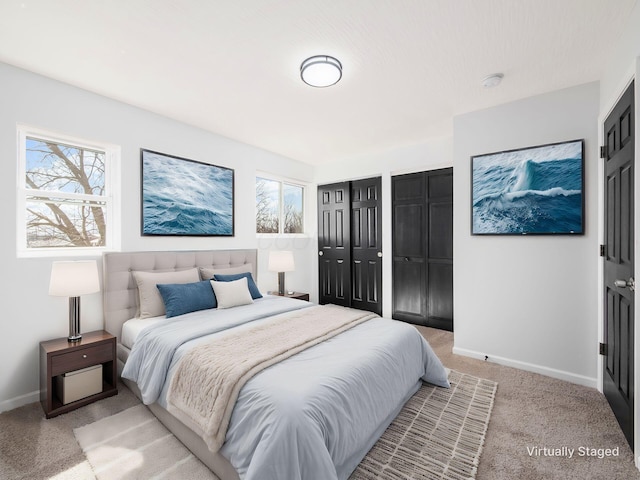 bedroom featuring light colored carpet, two closets, and baseboards