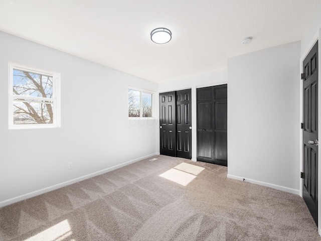 unfurnished bedroom featuring baseboards, multiple closets, and carpet