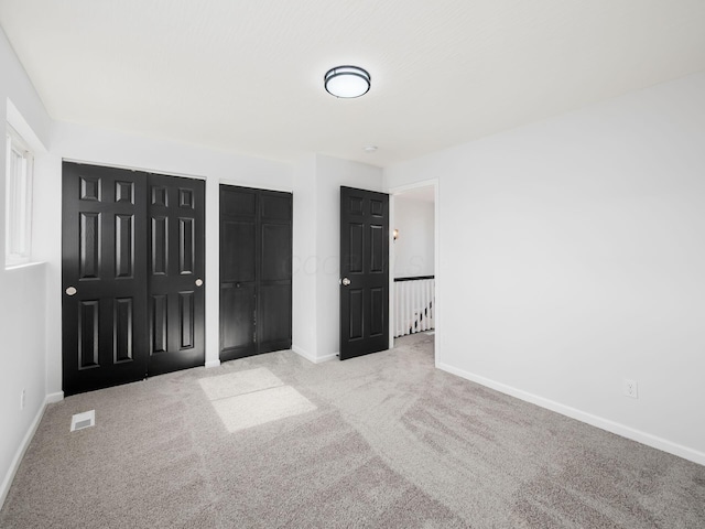 unfurnished bedroom featuring visible vents, baseboards, multiple closets, and carpet floors