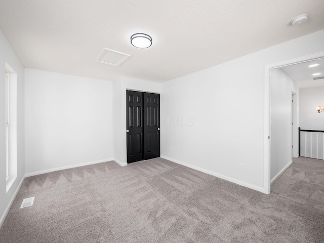 carpeted spare room featuring attic access, baseboards, and visible vents