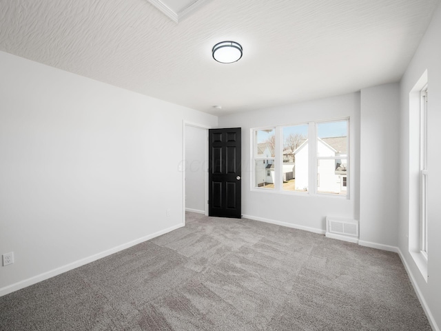 carpeted spare room featuring visible vents, a textured ceiling, and baseboards