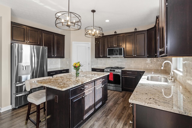 kitchen with dark brown cabinets, a center island, appliances with stainless steel finishes, an inviting chandelier, and a sink