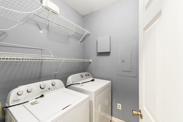 clothes washing area with electric panel, a textured ceiling, laundry area, and washer and clothes dryer