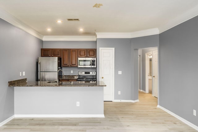 kitchen with dark stone countertops, a peninsula, a sink, ornamental molding, and stainless steel appliances