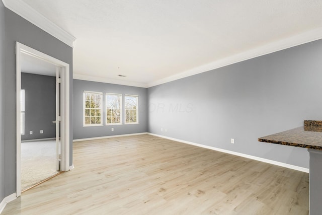 spare room with crown molding, baseboards, and light wood finished floors