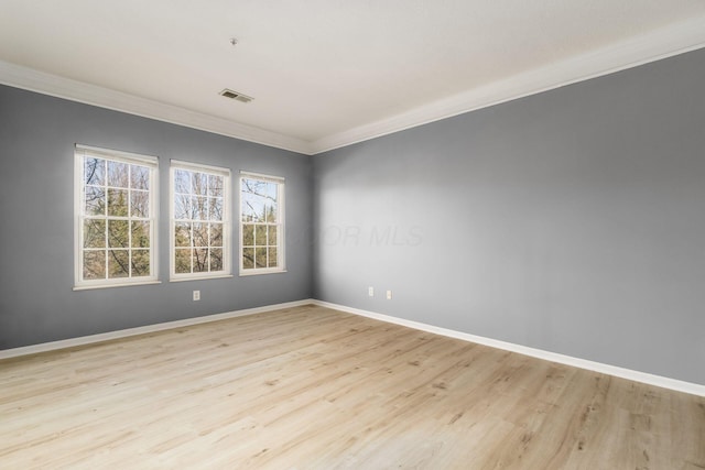 empty room with crown molding, light wood-style flooring, baseboards, and visible vents