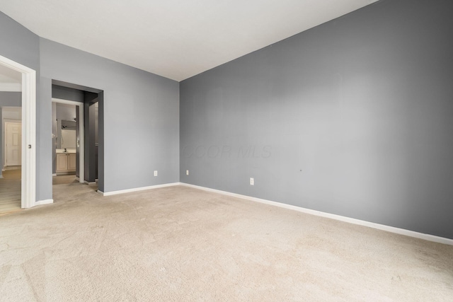 unfurnished bedroom featuring baseboards, light carpet, ensuite bathroom, and vaulted ceiling