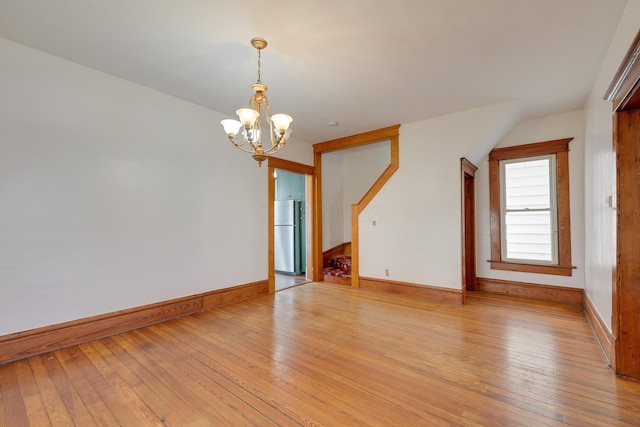 unfurnished room with light wood finished floors, a notable chandelier, and baseboards