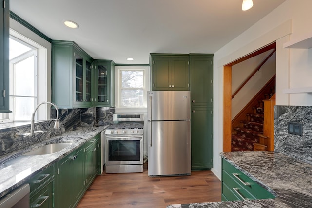 kitchen featuring green cabinetry, backsplash, appliances with stainless steel finishes, and a sink