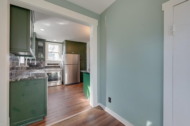 kitchen with green cabinetry, dark wood-style flooring, a sink, stainless steel appliances, and backsplash