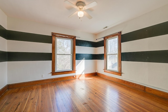 empty room with baseboards, wood-type flooring, visible vents, and ceiling fan