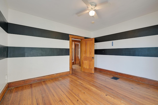 unfurnished room with hardwood / wood-style floors, a ceiling fan, visible vents, and baseboards