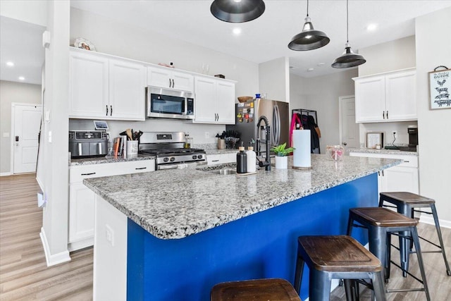 kitchen with a kitchen bar, a center island with sink, a sink, appliances with stainless steel finishes, and white cabinets