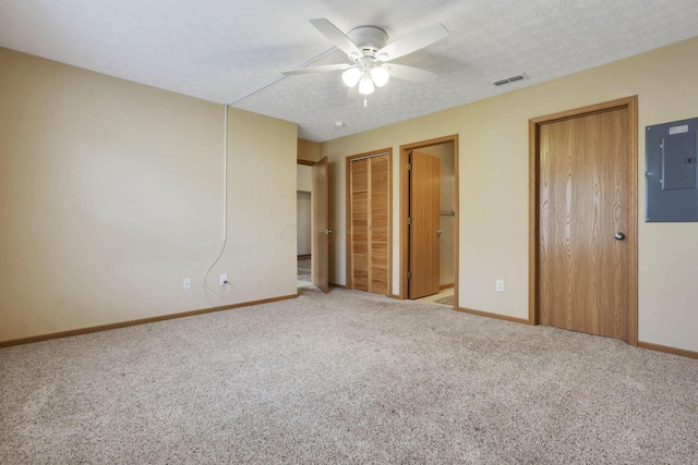 unfurnished bedroom featuring visible vents, electric panel, a textured ceiling, carpet flooring, and two closets