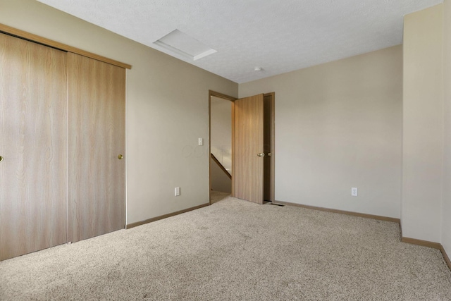 unfurnished bedroom featuring baseboards, attic access, carpet flooring, a closet, and a textured ceiling