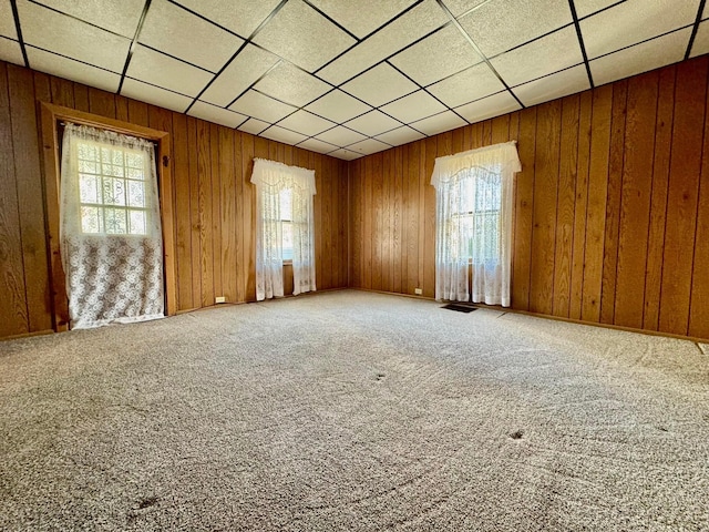 carpeted empty room with visible vents, a paneled ceiling, and wood walls