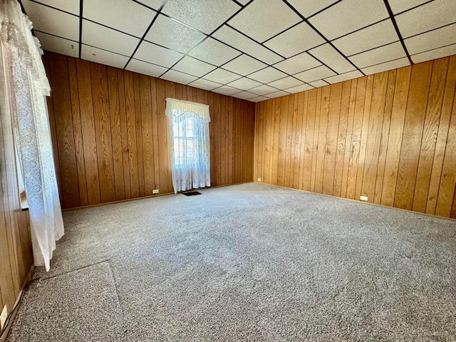 empty room featuring a drop ceiling, carpet, visible vents, and wood walls