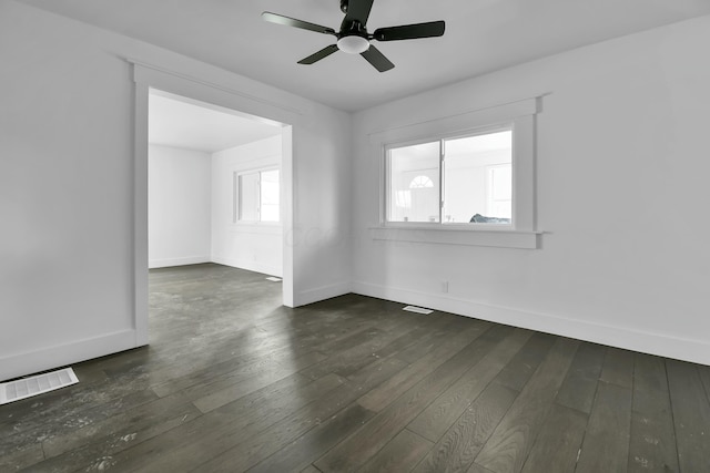 spare room featuring dark wood-type flooring, a ceiling fan, visible vents, and baseboards