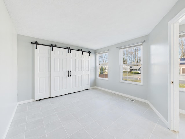 unfurnished bedroom with visible vents, baseboards, and a barn door