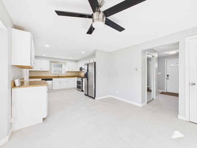 kitchen with ceiling fan, a sink, stainless steel appliances, white cabinets, and backsplash