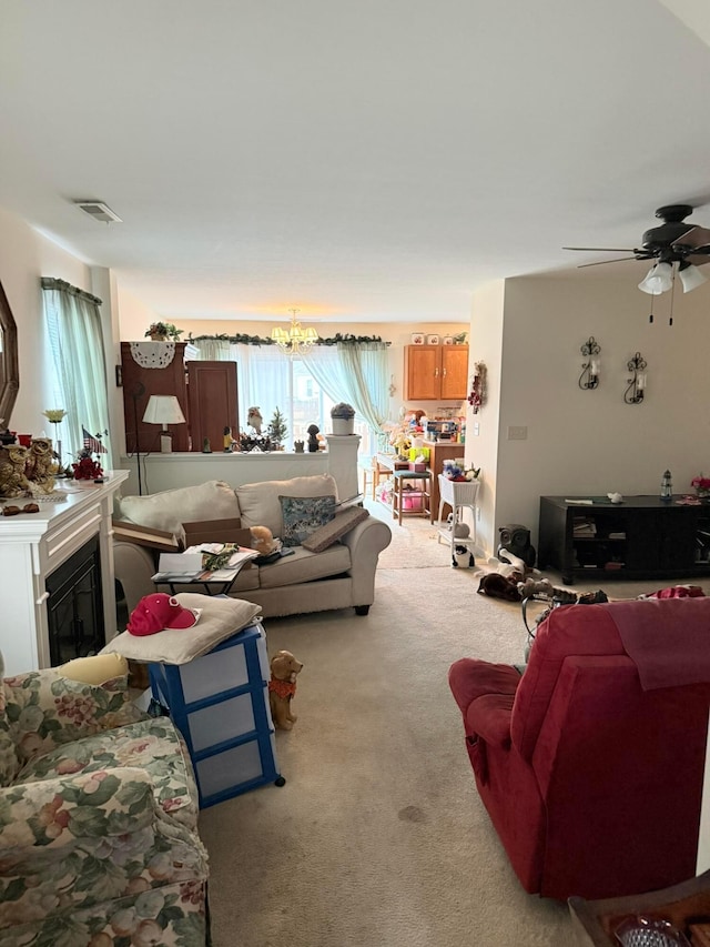 living room with ceiling fan with notable chandelier, a glass covered fireplace, carpet, and visible vents