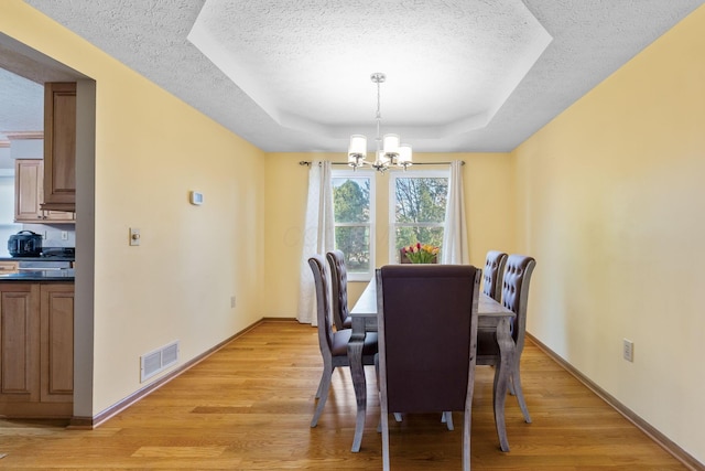 dining area featuring a notable chandelier, visible vents, light wood finished floors, and a raised ceiling