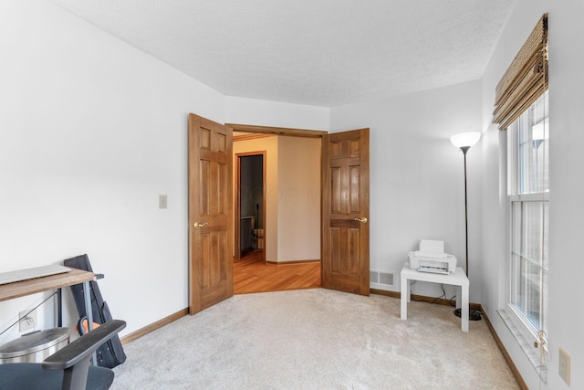 interior space with visible vents, light colored carpet, baseboards, and a textured ceiling