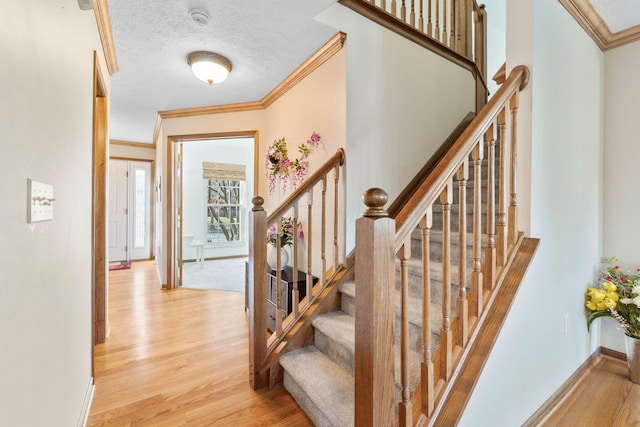 stairway with crown molding, wood finished floors, baseboards, and a textured ceiling