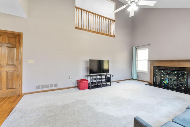 living room featuring visible vents, a fireplace with flush hearth, a high ceiling, baseboards, and ceiling fan