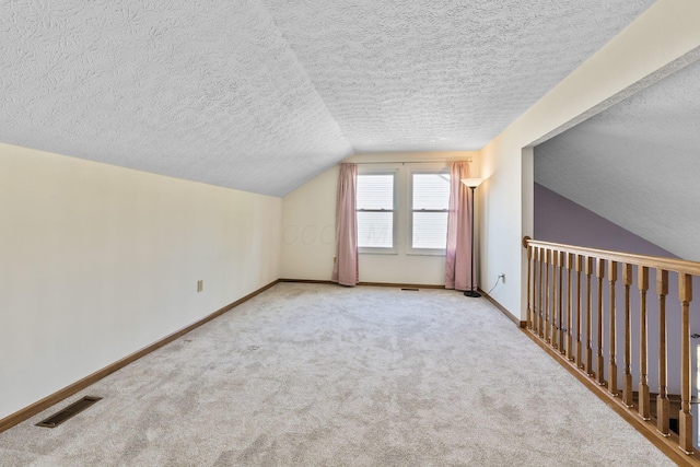 additional living space with baseboards, visible vents, vaulted ceiling, a textured ceiling, and carpet flooring