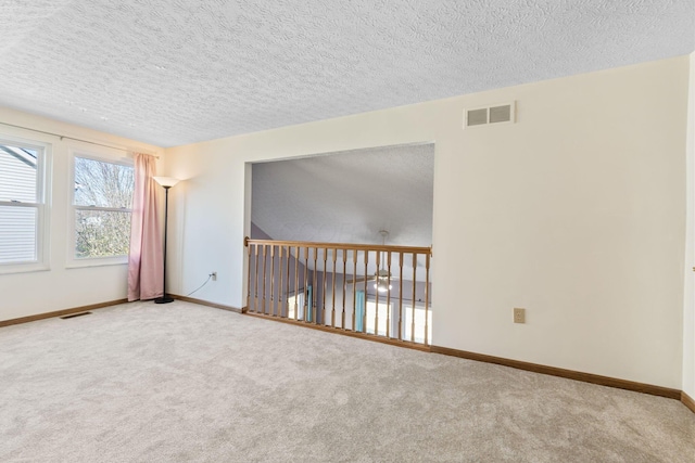 carpeted spare room featuring baseboards, visible vents, and a textured ceiling