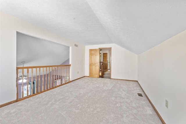 additional living space featuring carpet, baseboards, visible vents, lofted ceiling, and a textured ceiling