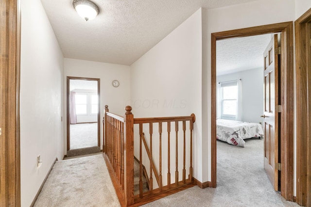 corridor featuring an upstairs landing, carpet flooring, and a textured ceiling