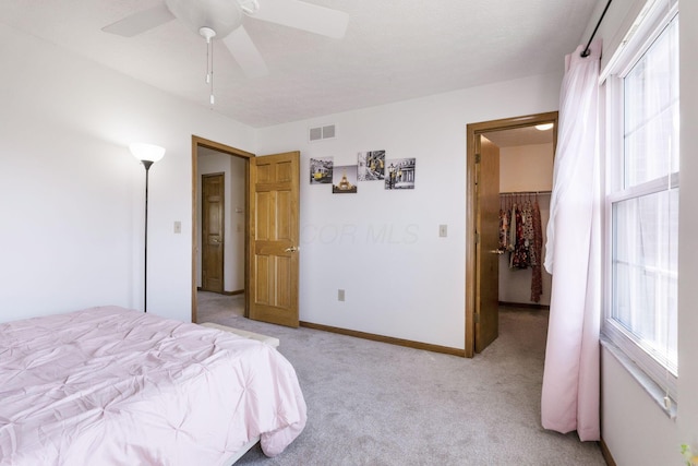 bedroom featuring visible vents, a walk in closet, a ceiling fan, baseboards, and light colored carpet