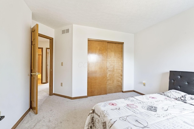 bedroom featuring light carpet, visible vents, a textured ceiling, and baseboards