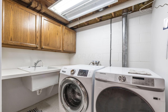 washroom featuring a sink, concrete block wall, cabinet space, and washing machine and clothes dryer