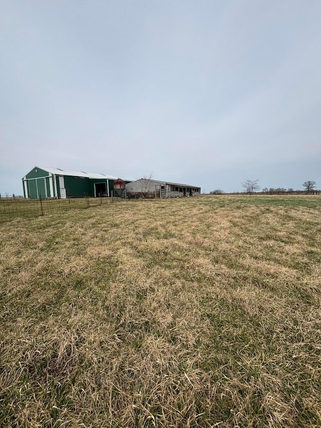 view of yard featuring an outbuilding, a rural view, an outdoor structure, and fence