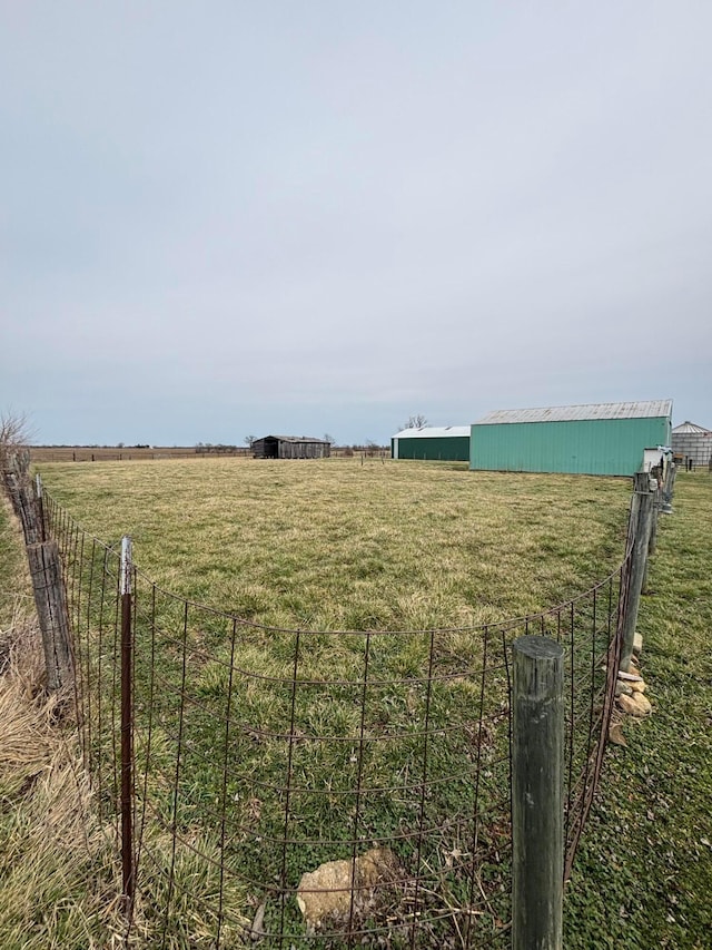 view of yard with a rural view, an outbuilding, and fence