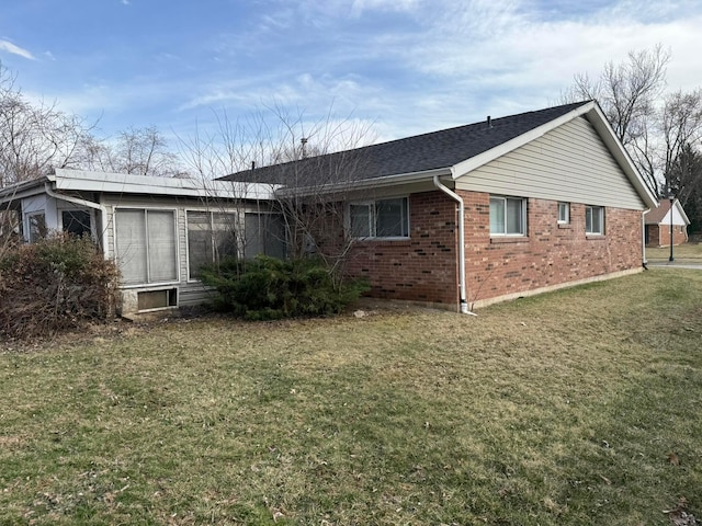 rear view of property featuring brick siding, a shingled roof, and a yard